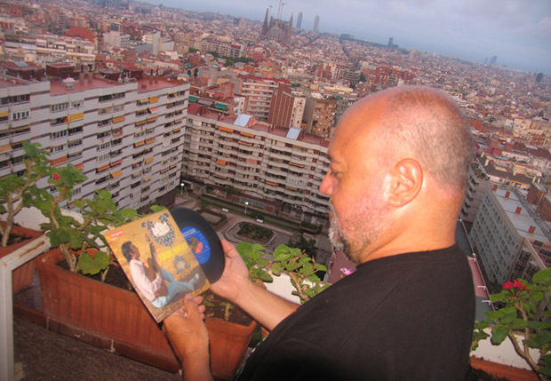 Fermí Puig en la terraza de su casa observando el primer single de su colección, el «Mig amic» (Vergara, 1968) de Peret. Al fondo, la Barcelona que tanto ha cantado Serrat. © Manel Gausachs